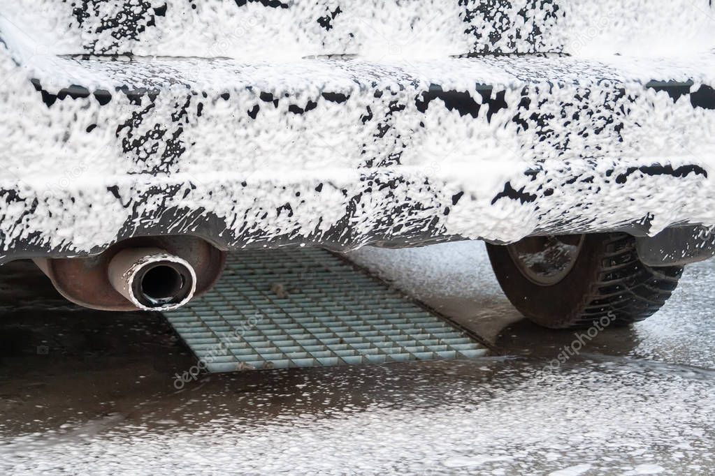 Black car being covered in foam on the self-service car wash. Close-up on the rear bumper, exhaust pipe and wheel