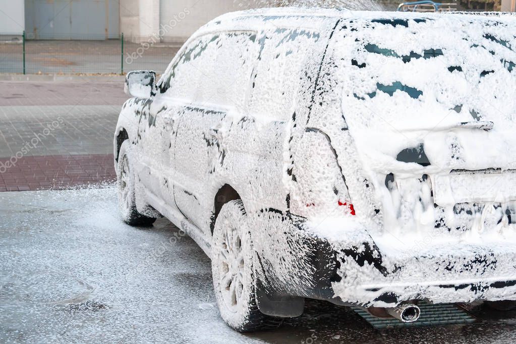 Black car being covered in foam on the self-service car wash. Back and side view