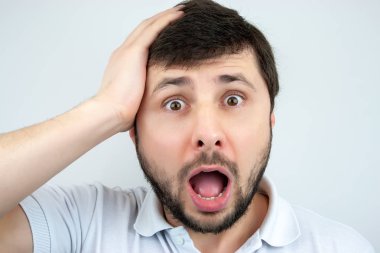 Elinde beyaz bir arka plan üzerinde beyaz bir T-shirt ile başını tutan bir sürpriz sakallı adamın gözleri ve ağzı açık, portre