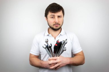 A bearded man with narrowed one eye in a white t-shirt with a bouquet of wrenches and screwdrivers clipart