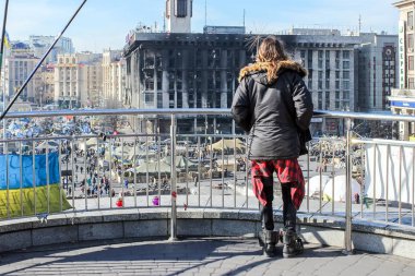 Jared Leto, metal bir çit tarafından ayakta, bir yanmış bina ve Maidan Nezalezhnosti üzerinde Euromaidan zamanlarında bir çadır şehir aşağı bakıyor