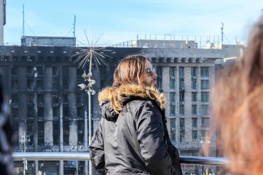Jared Leto, metal bir çit tarafından ayakta, bir yanmış bina ve Maidan Nezalezhnosti üzerinde Euromaidan zamanlarında bir çadır şehir aşağı bakıyor