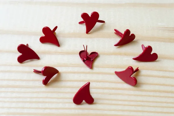 A circle of metal hearts on a wooden background. One in the center is turned