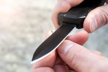 Erkek ellerinin, siyah bir cebi olan küçük ince ahşap bir çubuğu keskin bir bıçakla ön bıçakla keskinleştirmesinin yakın görünümü. Bulanık arka plan