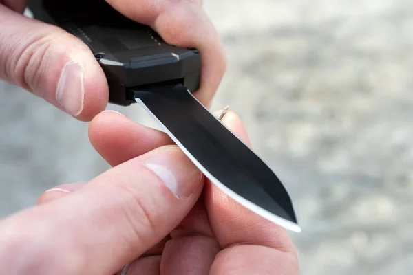 Erkek ellerinin, siyah bir cebi olan küçük ince ahşap bir çubuğu keskin bir bıçakla ön bıçakla keskinleştirmesinin yakın görünümü. Bulanık arka plan