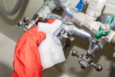 Kırmızı eldivenli bir el beyaz melamin sünger ile kireçtaşı ile kaplı krom kaplama musluk ovuşturuyor. Seçici odak. Yakın çekim görünümü