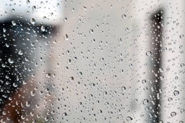 Bulutlu bir günde bulanık bir arka planda cam üzerindeki su damlaları