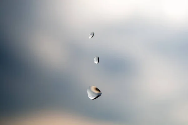 Three drops of rain of different size on the glass against a cloudy blurred sky background