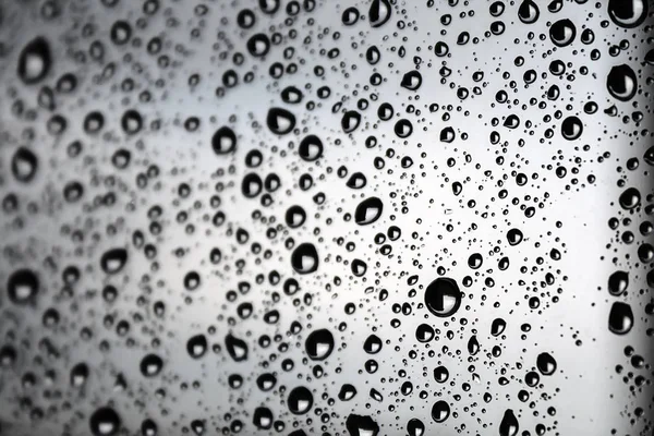 Чорні краплі води з білим сяйвом на склі на тлі розмитого хмарного неба в дощовий день. Вибірковий фокус — стокове фото