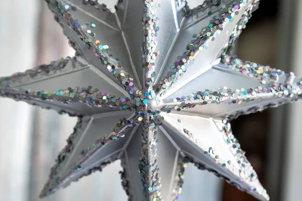 Крупный план серебряной рождественской звезды с множеством разноцветных шестиугольных блесков по краям. Новогоднее украшение дома. Рождественская ёлка — стоковое фото