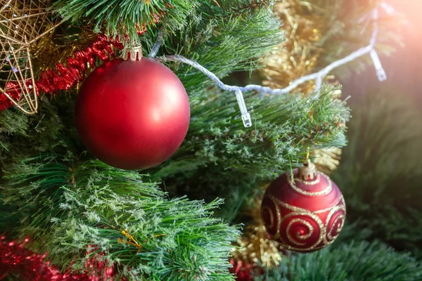 Arbre de Noël artificiel vert décoré de deux boules rouges : mat et paillettes ; et guirlandes jaunes et rouges. Décoration de maison pour des vacances en famille. Concentration sélective — Photo