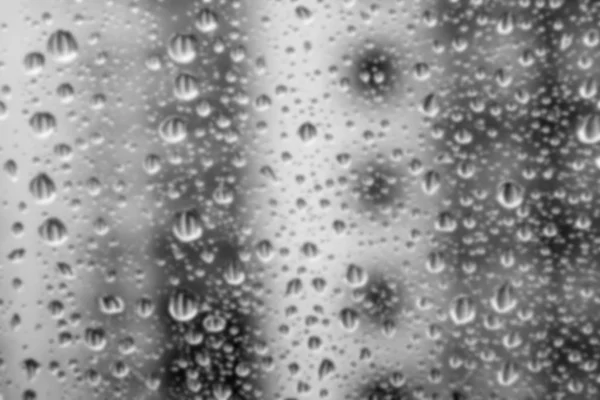 Defocused drops of water on the window glass against a blurred background of a house on a rainy cloudy day. Black and white drops of different sizes reflect the neighboring apartment building — Stock Photo, Image