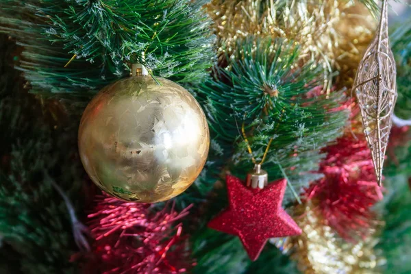 Зеленая искусственная елка украшена красивым золотым шаром, красными и золотыми гирляндами и другими игрушками. Оформление дома для семейного праздника. Селективный фокус — стоковое фото