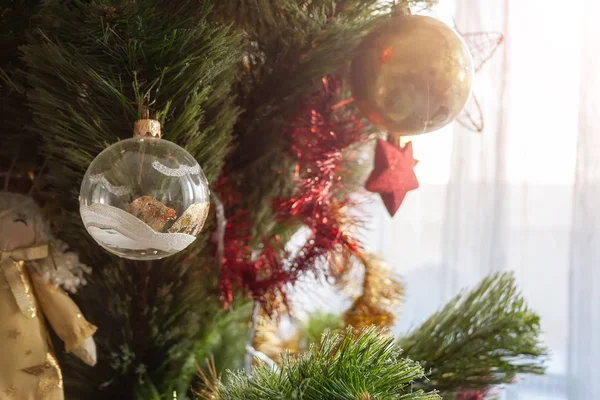 Zelený umělý vánoční stromek zdobený průhlednou koulí s bílými a zlatými vzory a dalšími hračkami pro rodinné svátky. Selektivní zaměření — Stock fotografie