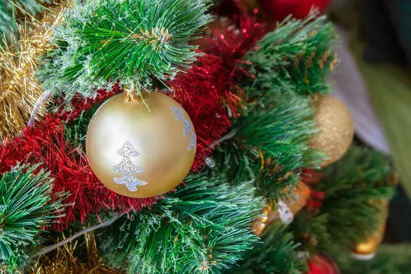 Arbre de Noël artificiel vert décoré d'une belle boule dorée avec des paillettes d'argent, des guirlandes rouges et dorées et d'autres jouets. Concentration sélective — Photo
