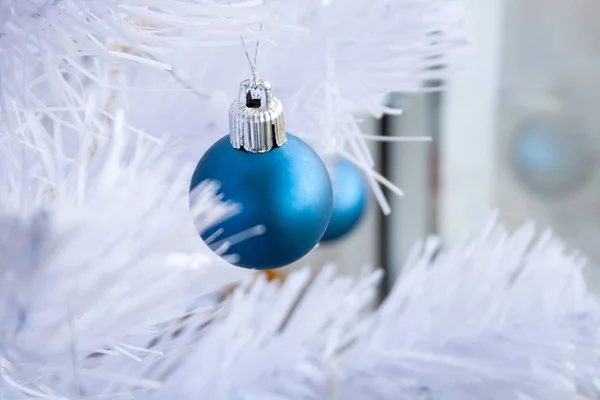 Nahaufnahme einer blau-matten Kugel, die an einem silbernen Faden an einem weißen künstlichen Weihnachtsbaum hängt. Selektiver Fokus. verschwommener Hintergrund — Stockfoto