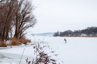 Adam uzakta karlı donmuş bir nehirde balıkçılık için bir delik sıkıcı. Kış manzarası