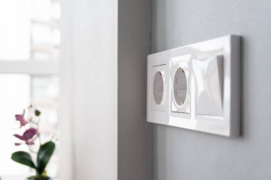 Beyaz Avrupa elektrik prizlerinden oluşan bir grubun yakından görünümü ve pencerenin yanında açık ve modern bir mutfakta gri bir duvarda bulunan bir anahtar. Seçici odak. Bulanık arka plan