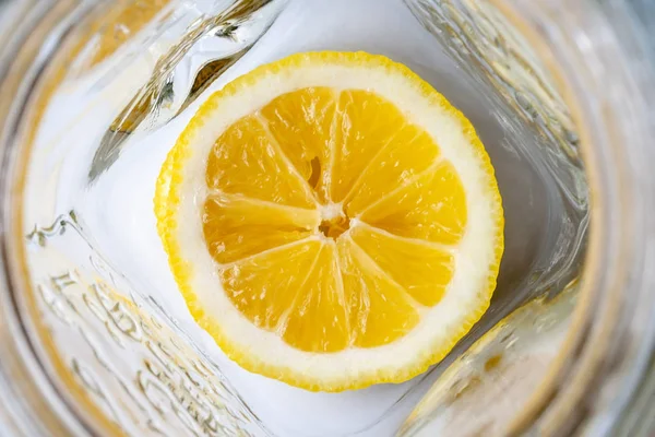 Boş bir cam kupanın dibinde parlak sarı dilimlenmiş limon. Güneşli bir sabah kahvaltı için limonata malzemeleri. Seçici odak. Üstte görüntü