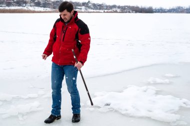 Kırmızı ceketli ve kot pantolonlu bir adam donmuş nehirde levyeyle yumruklanan buzdan memnun görünmüyor.
