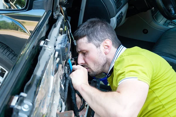 Człowiek w zielonym t-shirt uważnie demontuje drzwi samochodu w celu naprawy okna zasilania. Naprawa samochodów na stacji serwisowej przez wykwalifikowanego pracownika. Szukanie problemu w wadliwym samochodzie — Zdjęcie stockowe