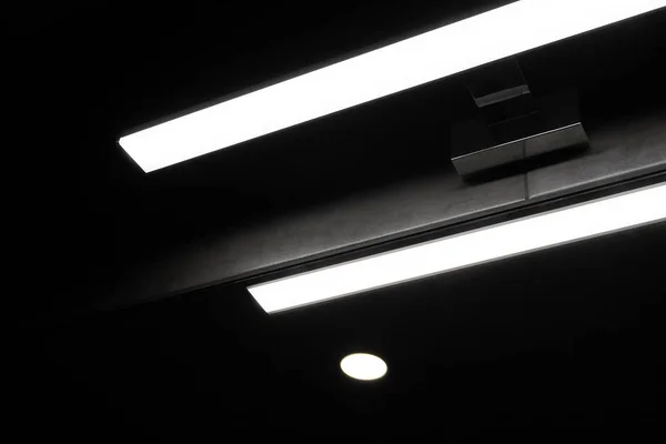 Un juego de luces y sombras con una moderna lámpara de pared en forma de una larga franja, que se refleja en un espejo en una habitación oscura. Formas geométricas abstractas diagonales y líneas. Negro, blanco, gris foto —  Fotos de Stock