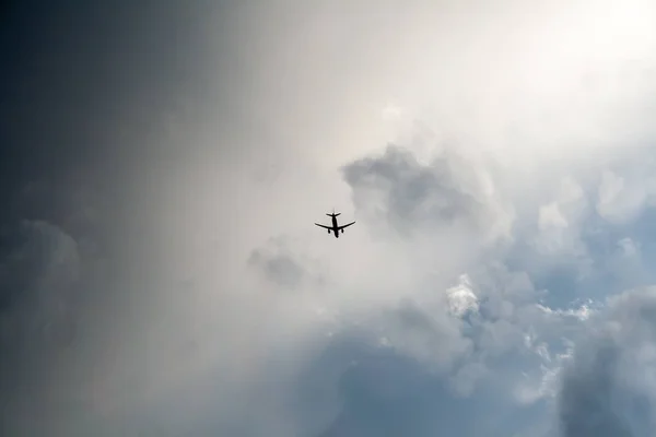 A small black silhouette of a flying airplane against a dramatic cloudy dark blue sky. Thunderstorm flights. Non-flying weather — Stock Photo, Image