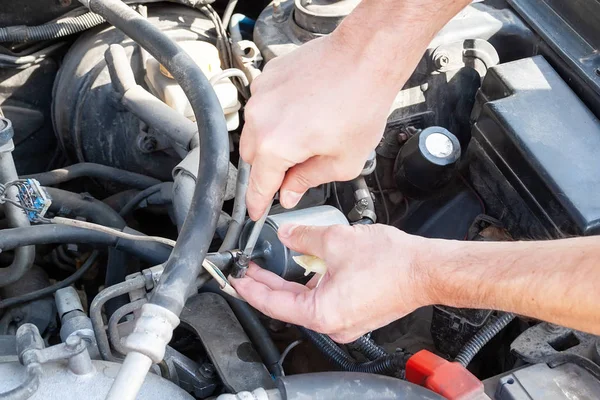 Mannelijke handen schroef de brandstofleiding uit het brandstoffilter met een Phillips schroevendraaier om het te vervangen. Reparatie en vervanging van auto-onderdelen in een servicecentrum — Stockfoto