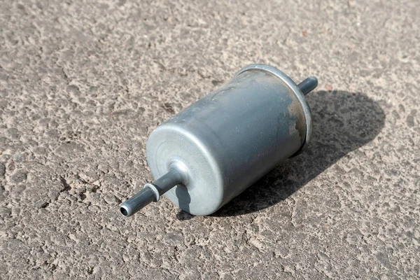 Used fuel filter on a gray asphalt on a sunny day. Filter element in the fuel line that traps particles of dirt and rust from the gasoline