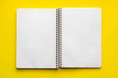 Parlak sarı bir zemin üzerinde boş beyaz sayfaları ile spiral defter aç, üst görünüm, düz yatıyordu