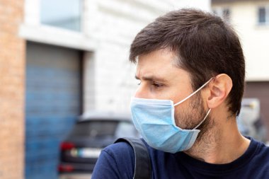 Kordemik Coronavirus covid-19 döneminde mavi maske takmış somurtkan beyaz bir adamın sokak portresi. Virüslü enfeksiyondan korunmak için tek kullanımlık solunum cihazında bir erkek.
