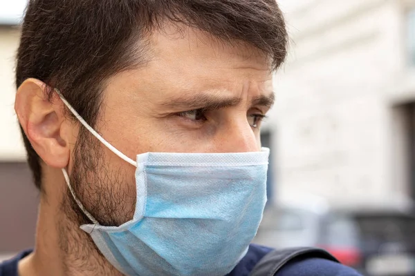 Kordemik Coronavirus covid-19 döneminde mavi maske takmış somurtkan beyaz bir adamın sokak fotoğrafı. Virüslü enfeksiyondan korunmak için tek kullanımlık solunum cihazında bir erkek.
