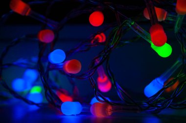 Karanlıkta bükülmüş siyah bir kordon üzerinde mavi, yeşil ve kırmızı küçük Noel mat ışıkları. Herhangi bir tatilde ev dekorasyonu için aydınlatma. Seçici odaklanma. Bulanık arkaplan