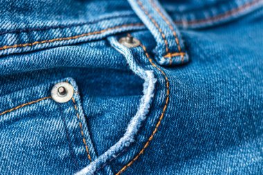 Cepleri ve perçinleri olan kot pantolonlar önde. Parlak mavi kot kumaş dokusu arka planı. Yakından bak. Seçici odak