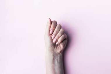 Güzel manikürlü bir kadın eli. Pembe arka planda küçük siyah noktalı pembe çıplak tırnaklar.