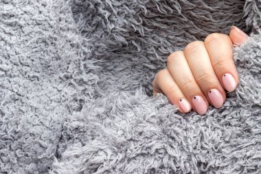 Gri, pofuduk, örülmüş, modaya uygun, güzel manikürlü süveterli bir kadın eli. Fotokopi alanı olan küçük siyah noktalı pembe çiviler. Seçici odaklanma. Yakın görünüm