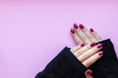 Siyah örgü eldivenli kadın elleri. Parlak manikürlü eldivenler. Bordo, pembe arka planda koyu kırmızı tırnaklar.