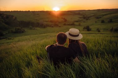 Şık genç çift bir tepede oturan ve gün batımı hayran. Bir ışık ve güneş ışığı ile bir film fotoğrafı, bir yüz olmadan