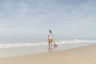 Küçük oğlu gri gün sahilde yürüyüş kadınla