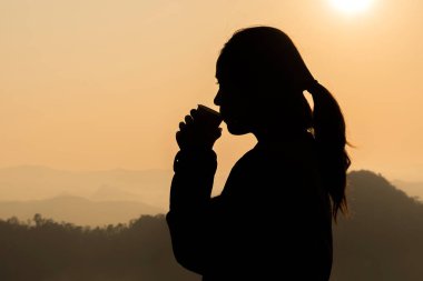 Karanlık dağlar turuncu zemin üzerine çay içme kadın silüeti.