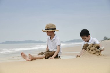 Kum ile kumsalda oynarken iki Asyalı çocuklar