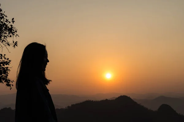 Dark silhouette of woman with sun on background with mountains.