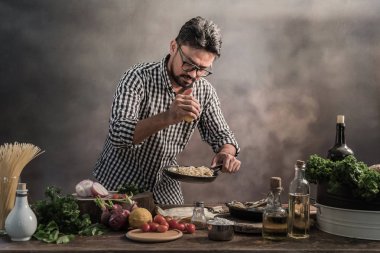 Sakallı genç mutfak spicing spagetti yemek.