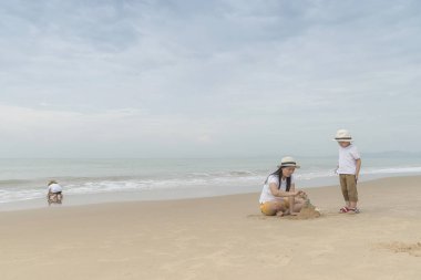 İki sevimli oğlu ile kumsalda oynarken annesi.