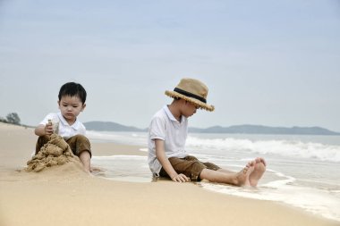 Sahilde kum ile birlikte oynayan iki Asyalı çocuklar