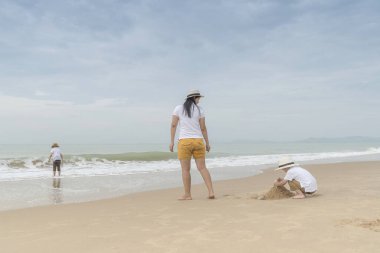 Kasvetli gün plajda iki oğlu ralaxing ile Asya Anne.