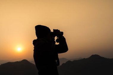 Throuh dürbün turuncu gökyüzü ve dağlar ile arka plan üzerinde görünen adam silüeti.