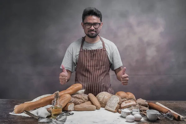 Asian man posing at table with buns and bread.