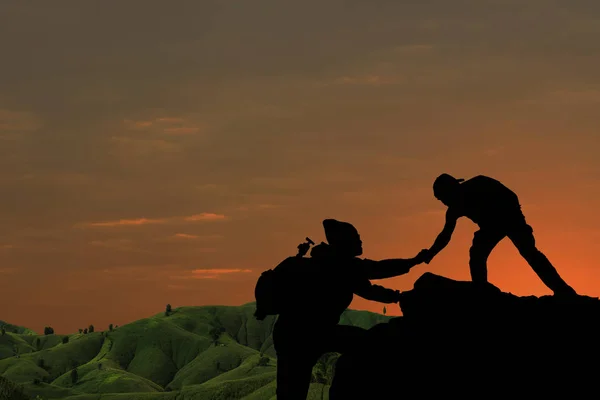 Friends helping each other trying to reach top of mountains during wonderful summer sunset.