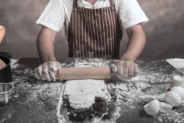 Cropped view of man preparing buns at table in bakery.